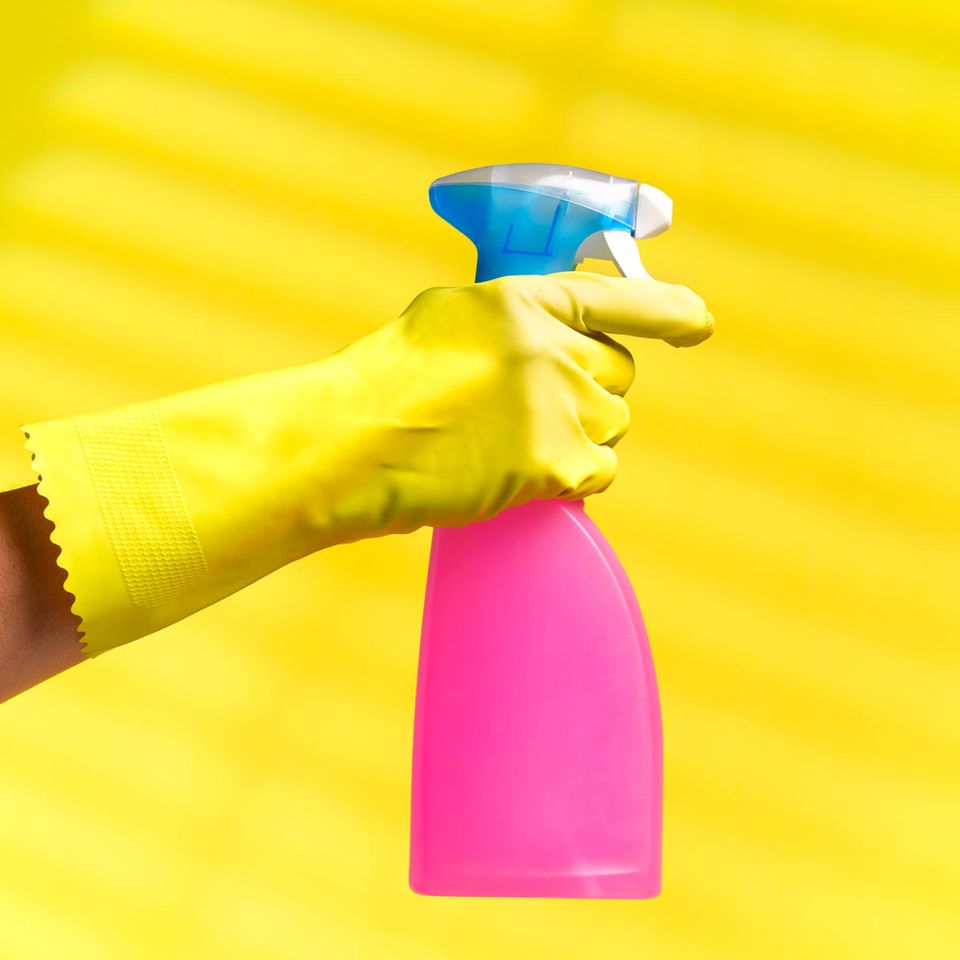 Sprühflasche und Putzhandschuh vor gelbem Hintergrund
