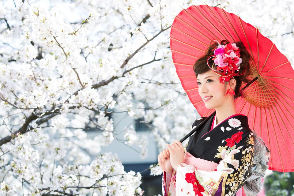 Anti-Stress-Tricks aus Japan: Eine japanische Frau mit Schirm vor einem Kirschbaum