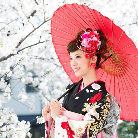 Anti-Stress-Tricks aus Japan: Eine japanische Frau mit Schirm vor einem Kirschbaum