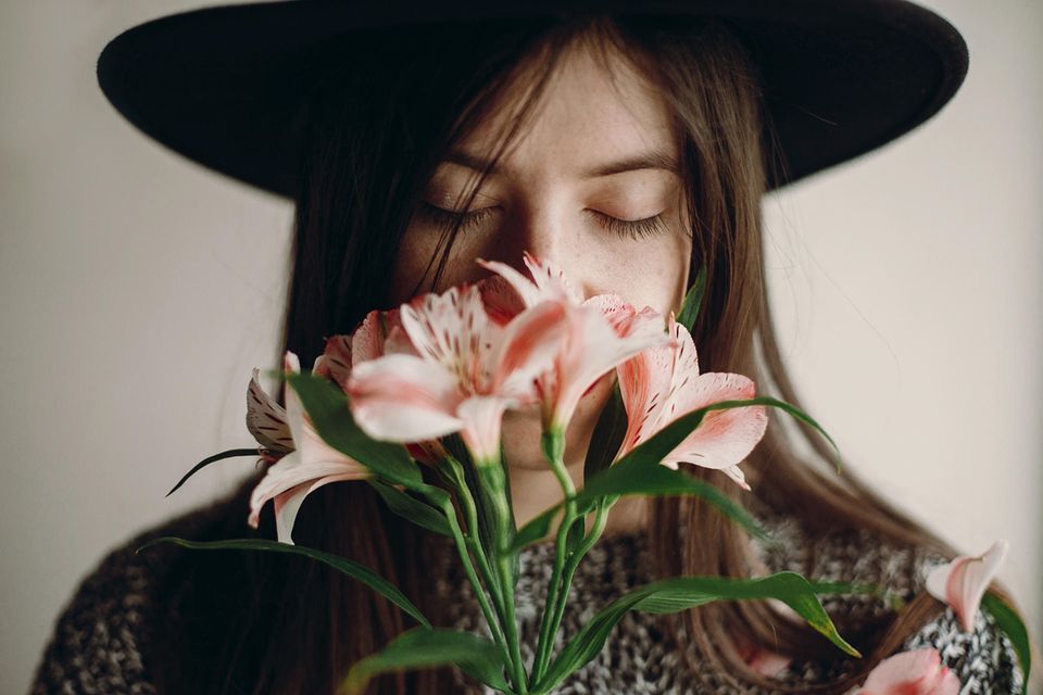 Anti-Komplimente: Frau mit Hut riecht an Blumen