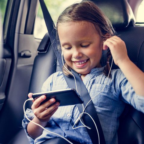Mädchen sitzt im Auto und hält Smartphone in der Hand