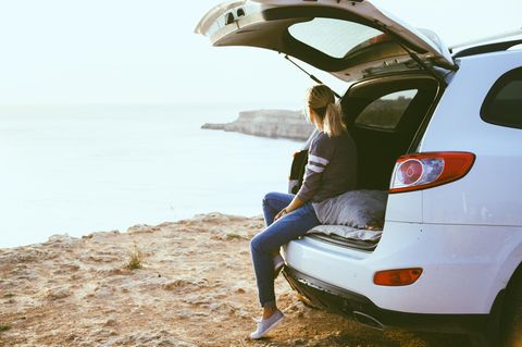 E-Auto: Eine Frau chillt im Kofferraum ihres Autos am Meer