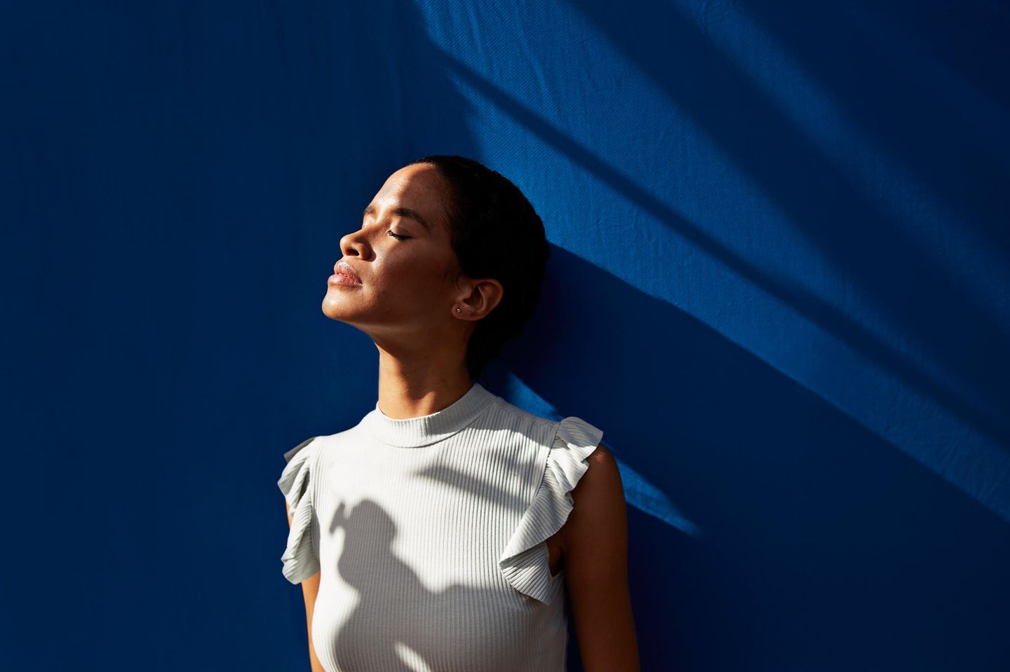 Frau vor blauem Hintergrund mit Gesicht zur Sonne