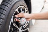 Spritsparend fahren: Frau kontrolliert Reifendruck