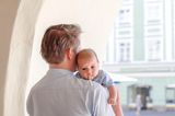 Familienleben: Vater trägt Baby auf dem Arm, welches sich auf sein Oberteil erbrochen hat