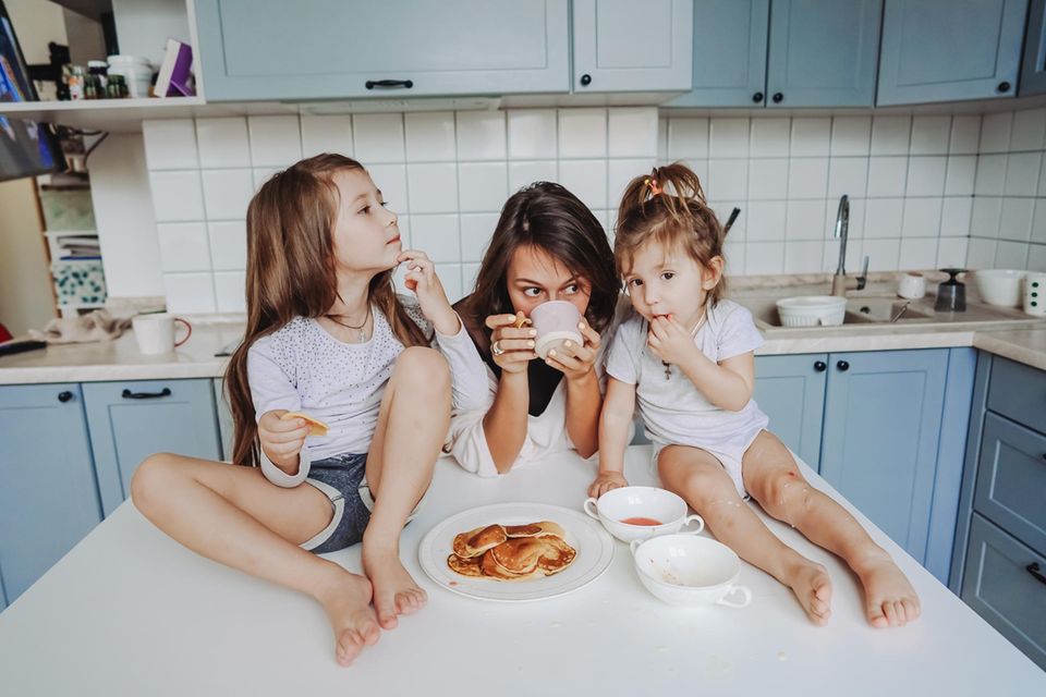 Mental Load: Mutter isst mit ihren zwei Kindern in der Küche