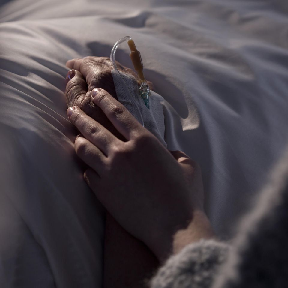 Abschied nehmen: Frau hält Hand eines Menschen am Sterbebett