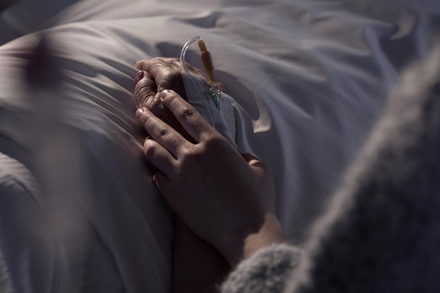 Abschied nehmen: Frau hält Hand eines Menschen am Sterbebett