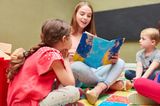 Kinderbetreuung: Junge Frau liest Kindern ein Buch vor