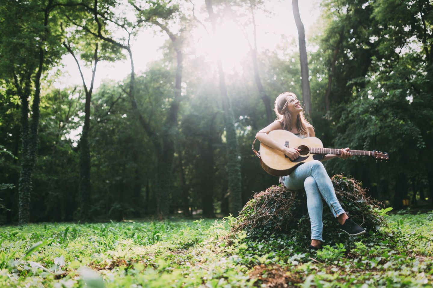 Eine Frau sitzt im Wald mit einer Gitarre