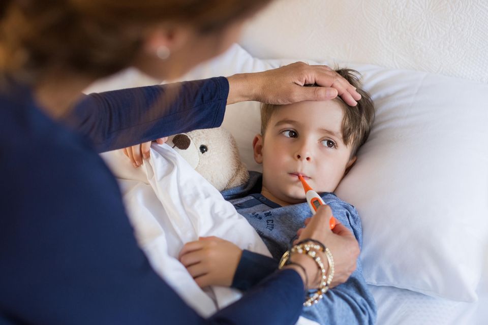 Husten, Schnupfen, Heiserkeit: Junge liegt mit Fieberthermometer im Bett