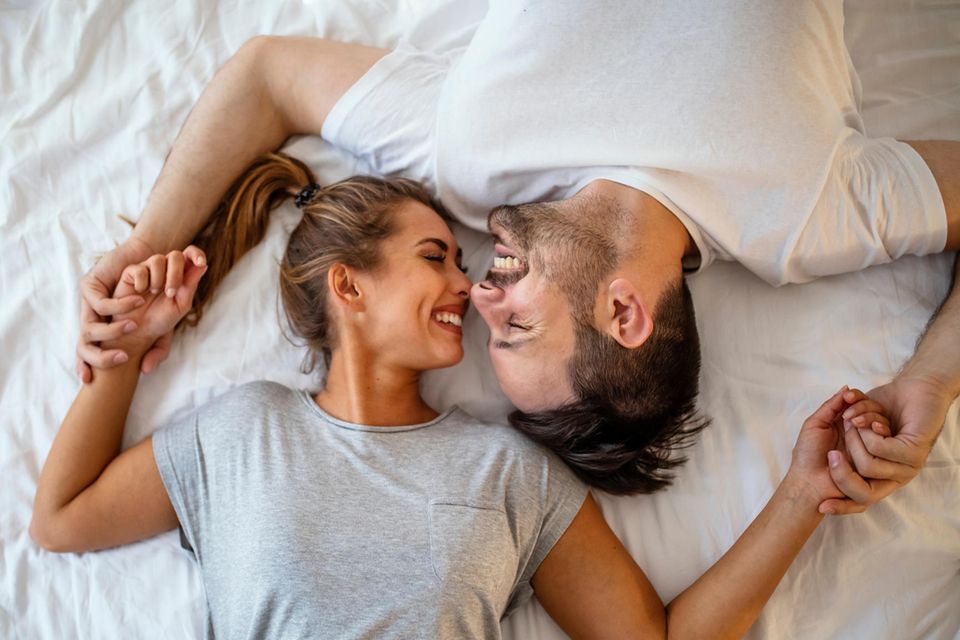 Karezza: Mann und Frau lächeln sich im Bett an