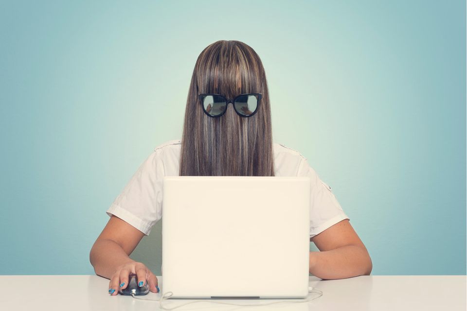 Frau mit Haaren und Brille vor dem Gesicht, sitzt am Laptop