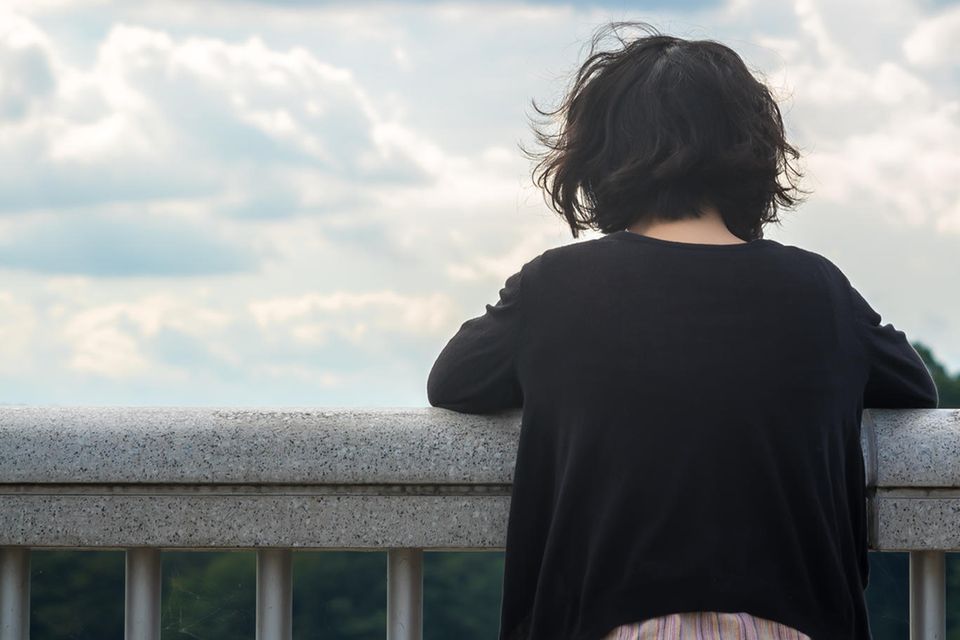 Suizidgedanken: Eine Frau steht am Geländer und denkt nach