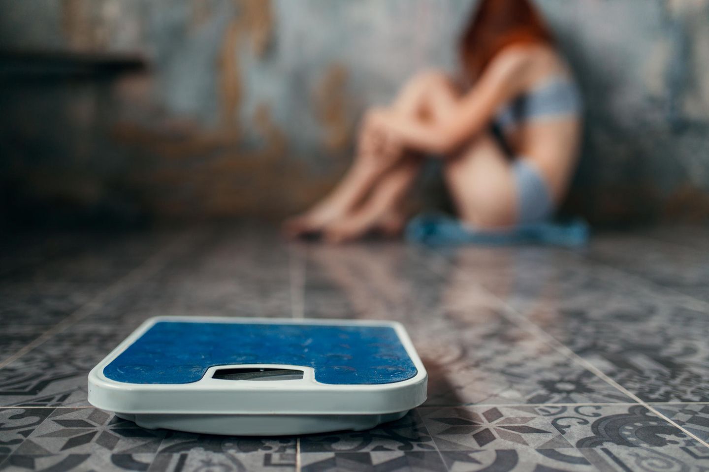 Magersucht: Mädchen kauert auf dem Boden, vor ihr eine Waage