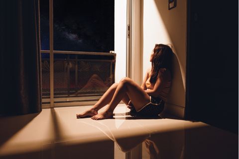 Hikikomori: Frau sitzt im Dunkeln am Fenster