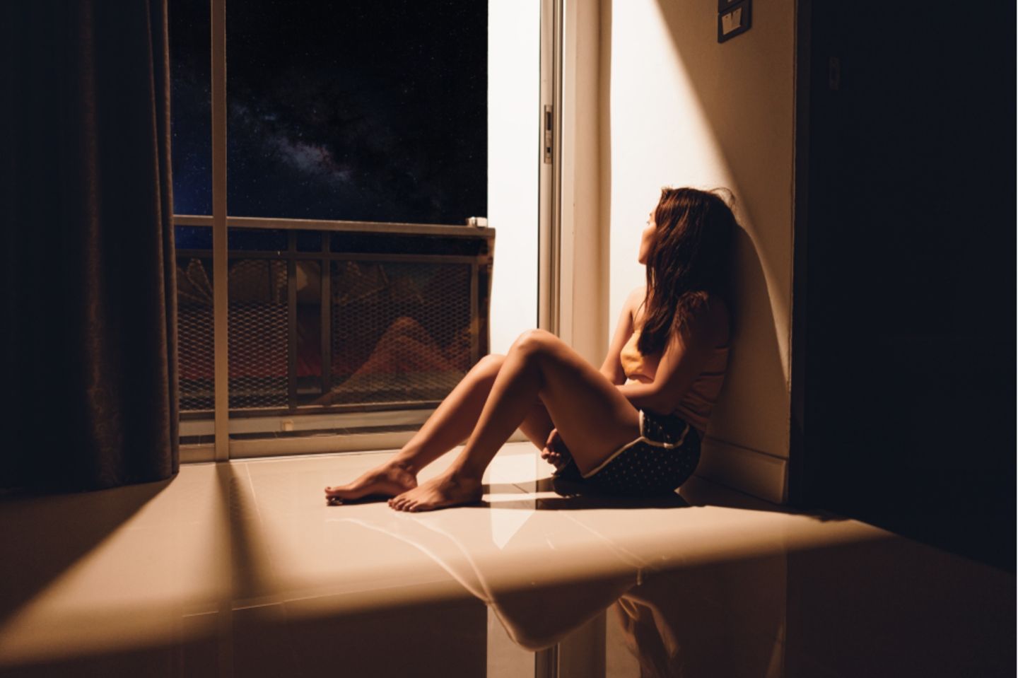 Hikikomori: Frau sitzt im Dunkeln am Fenster