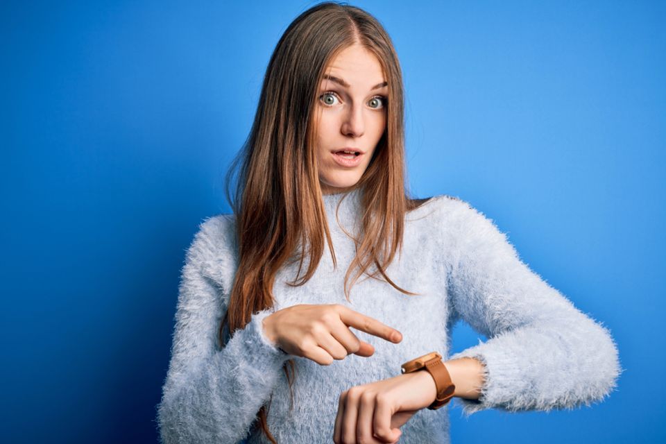 Ungeduld: Frau zeigt auf eine Uhr am Handgelenk.