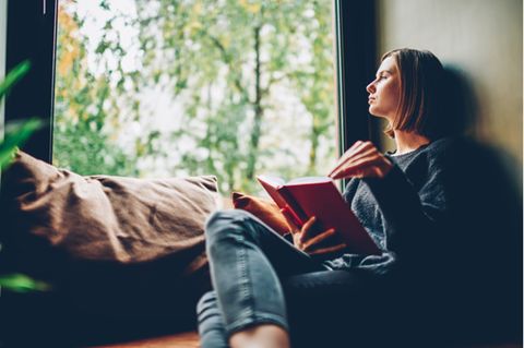 Bücher zum Nachdenken: Frau sitzt mit Buch auf der Fensterbank