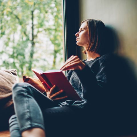 Bücher zum Nachdenken: Frau sitzt mit Buch auf der Fensterbank