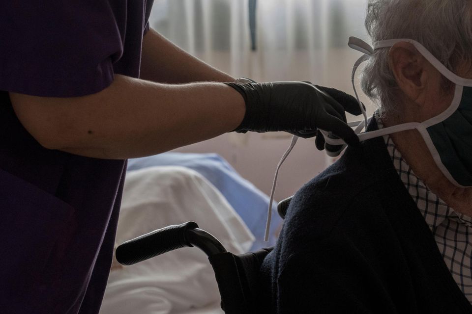 Corona aktuell: Eine Pflegerin hilft einer Seniorin mit dem Mundschutz
