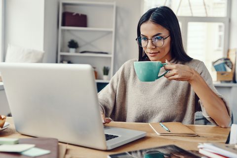 Home-Office-Tipps: Frau sitzt am Schreibtisch und hält Kaffeetasse in der Hand.