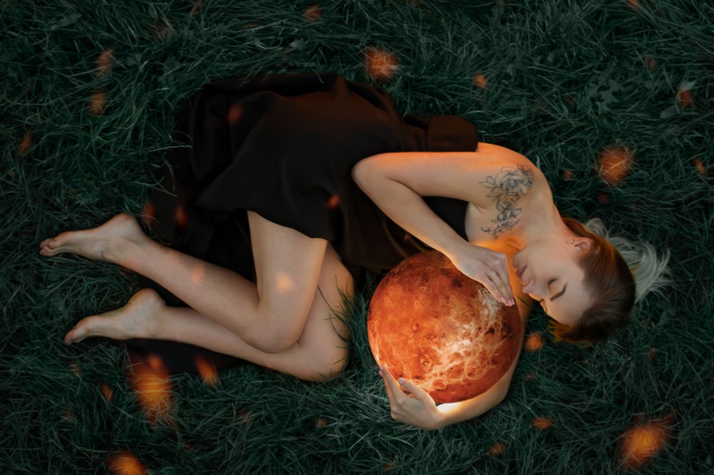 Venus Zeichen: Frau liegt auf der Erde und hält leuchtende Kugel in den Händen.