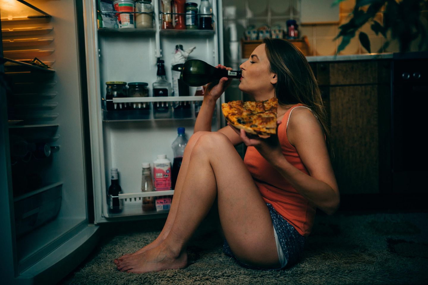 Frau sitzt vor Kühlschrank mit Pizza und Wein