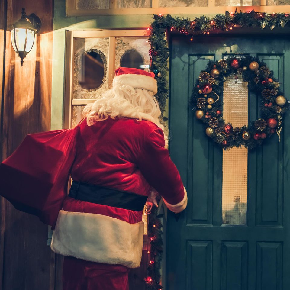 Weihnachtsmann mit Geschenken vorm Haus