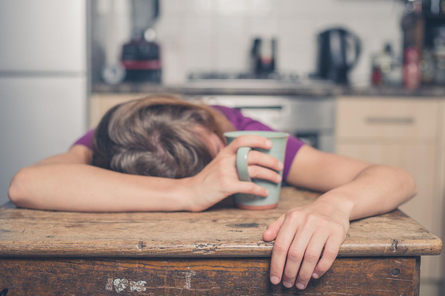 Narkolepsie: Frau schläft mit Tasse in der Hand auf dem Tisch