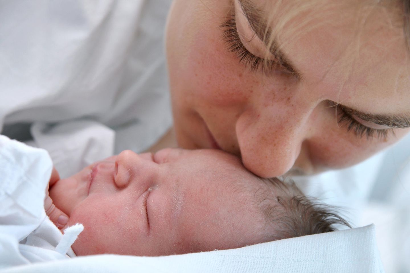 Die ersten Tage mit Baby: Mutter küsst Neugeborenes