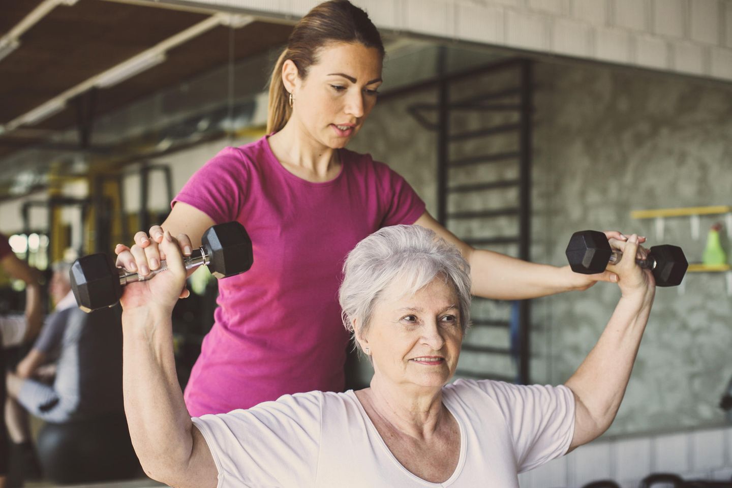Sport- und Fitnesskaufmann: Sport- und Fitnesskauffrau trainiert mit älterer Dame
