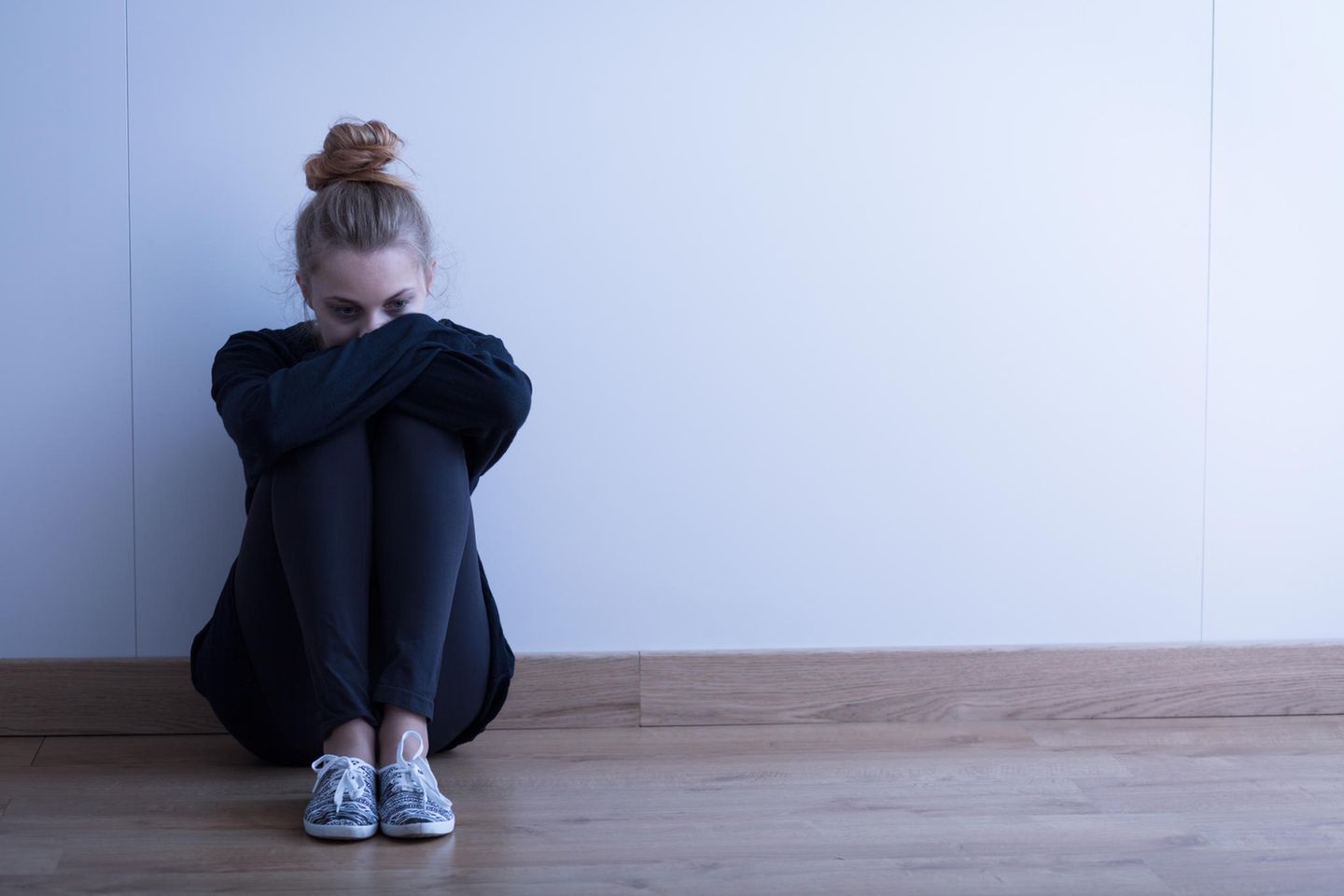 Psychologie: Eine junge Frau sitzt vor einer weißen Wand