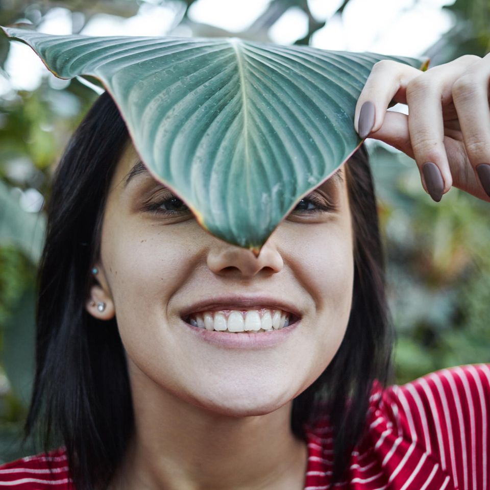 Green Beauty: Lächelnde Frau steht zwischen Pflanzen