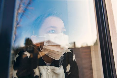 Kind mit Maske schaut aus dem Fenster