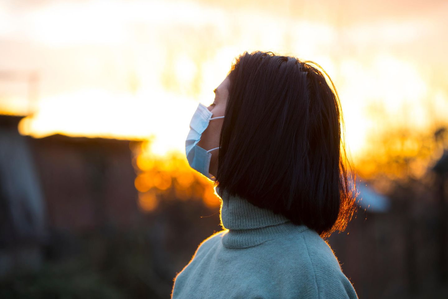 Corona aktuell: Frau mit Maske im Sonnenaufgang