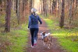 Eine Frau joggt mit ihrem Hund durch den Wald