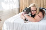 Bester Freund der Frau: Frau liegt auf Bett und umarmt Hund