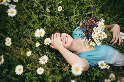 Horoskop: Eine lachende Frau liegt auf einer Blumenwiese