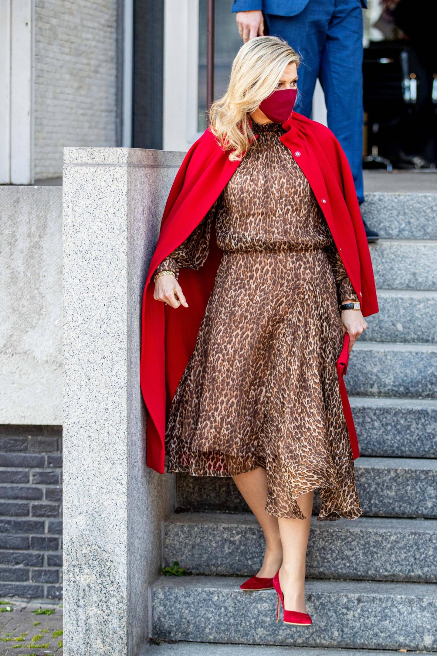 Königin Máxima schafft es, eine Kombi, die sonst fast zu sexy wäre, elegant aussehen zu lassen: Sie trägt ein leichtes Midi-Dress mit Leo-Muster, das an der Taille betont. Darüber hat sie sich einen knallroten Cape-Mantel (beides von Natan Couture) geworfen und ihre roten Pumps perfekt abgestimmt. 