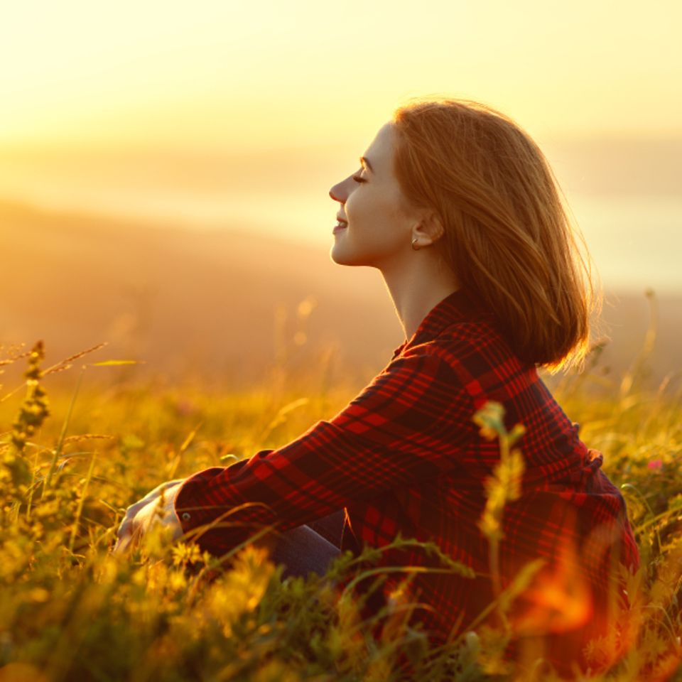 Selbstfindung: Frau sitzt in einem Feld vorm Sonnenuntergang