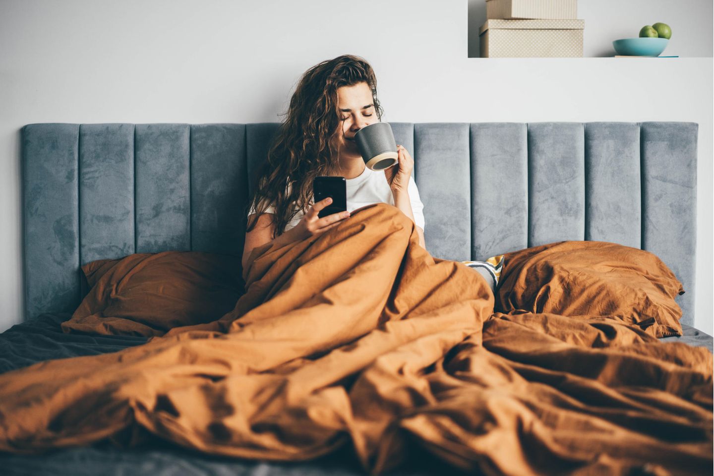 Zu viel am Smartphone? Social-Media-Experte rät: Frau im Bett mit Kaffee und Handy