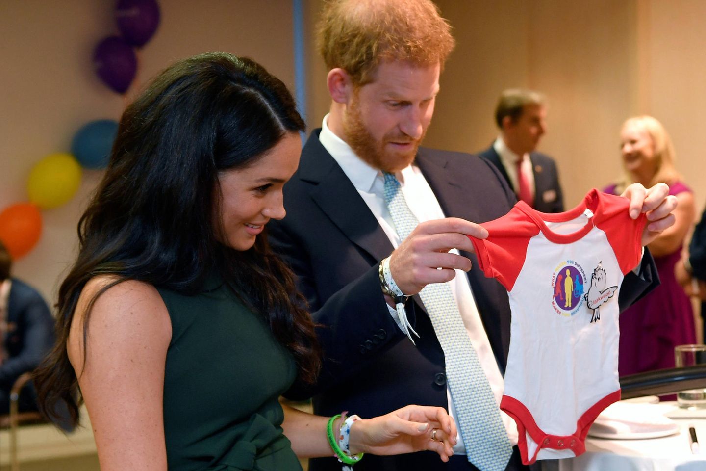 Herzogin Meghan + Prinz Harry: Dieser Titel steht ihrer Tochter zu: Beide stehen nebeneinander, Prinz Harry hält Strampler