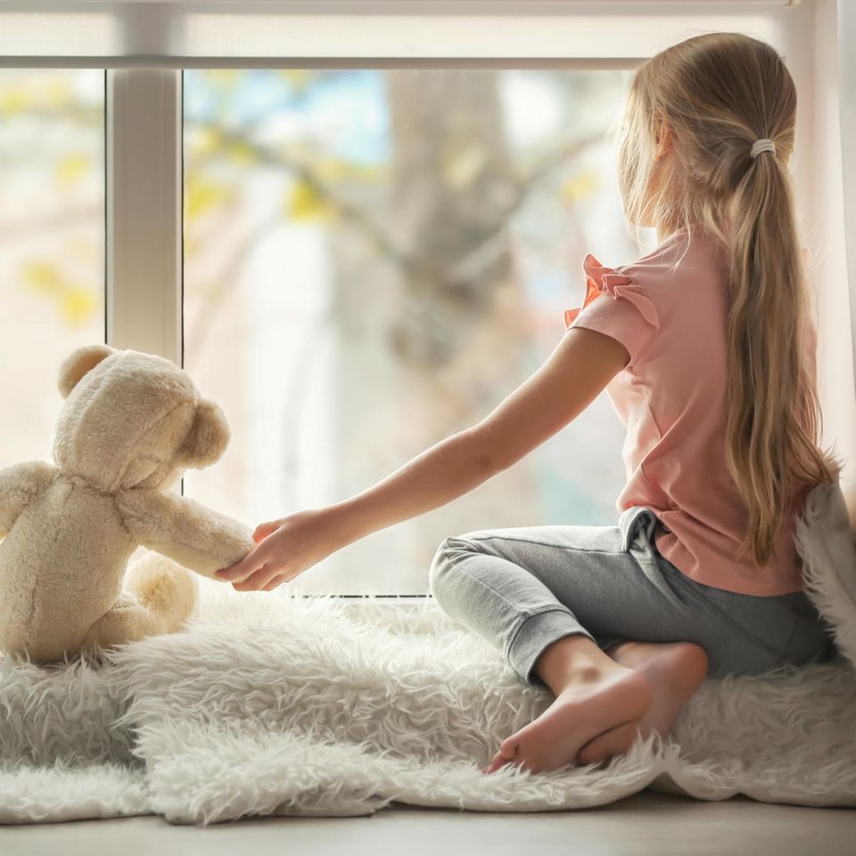 Kinderärzt:innen warnen: Mädchen sitzt vor einem Fenster