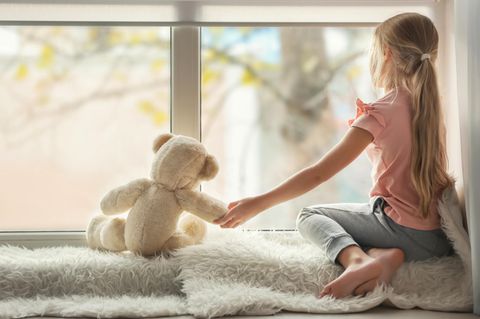Kinderärzt:innen warnen: Mädchen sitzt vor einem Fenster