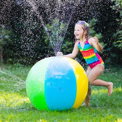 Wasserspielzeug: Mädchen in Badeanzug mit Wasserspielzeug im Garten, bunter Wasserball mit Düsen für Kinder