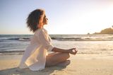 Horoskop: Eine Frau meditiert am Strand