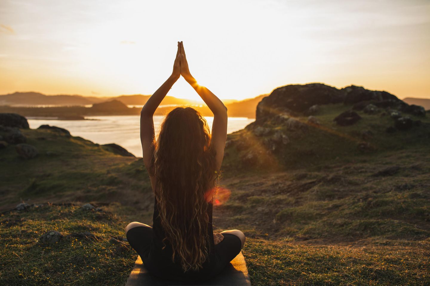 Horoskop: Eine Frau meditiert im Sonnenuntergang