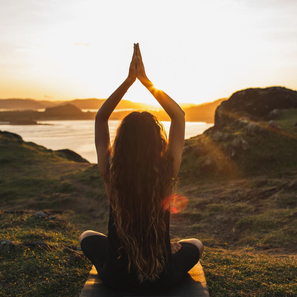 Horoskop: Eine Frau meditiert im Sonnenuntergang