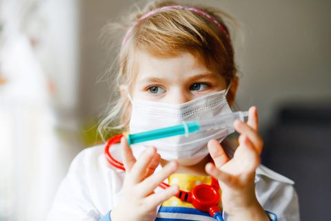Corona-Risiko bei Kindern: Mädchen mit Mund-Nasen-Schutz und Spritze